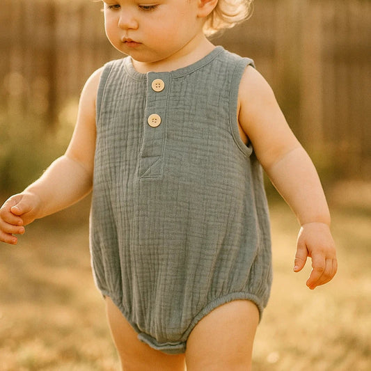 Child wearing a green sleeveless romper outdoors with a warm, blurred background